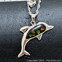 Close-up front view of sterling silver dolphin-shaped pendant with colorful gemstone inlay on black background.