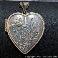 Front angled view of the sterling silver heart shaped locket pendant showing the intricate floral engraving and hinged side opening.