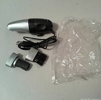 Mini USB vacuum cleaner shown with two attachments (brush and suction). USB cable attached for power.