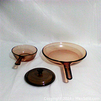 Two amber glass Vision Ware skillets with one lid on white background