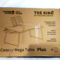 Photo of cardboard packaging featuring product branding and description. Shows desk illustration with drawer and notes it is foldable and multifunctional.