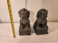 Two dark stone dragon statues side by side with measuring tape showing height around 8 inches.