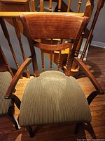 Front view of wooden dining armchair with curved slatted backrest, carved arms, upholstered striped seat on hardwood floor