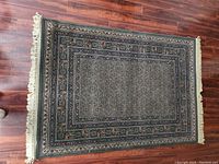 Top-down photo of a rectangular area rug measuring approximately 5'7" x 4'. Traditional Afghan pattern with fringe on shorter edges laid on wood floor.