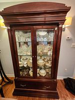 Front view of the wood china hutch showing glass doors with china inside, decorative top molding, and bottom drawer
