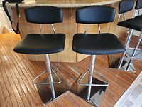 Four black adjustable barstools, two with damage on top of seat backs, metal square bases with footrests, placed in kitchen area