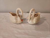 Front view of the set showing two swan-shaped porcelain items, a creamer and a sugar bowl, on a white surface.