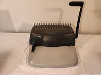 Front view of GBC binding machine showing punching pins and lever handle on white surface.