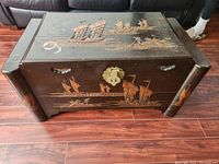 Front and side view of the dark wooden cedar lined chest decorated with hand-painted Asian sailing ships and fishermen scenes. Visible brass clasp and some wear marks.