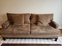 Front view of brown microfiber sofa with two seat cushions, two back cushions, two throw pillows, and black wooden legs.