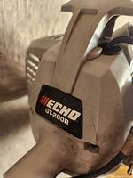 Close-up of Echo GT-200R branding on the engine casing, showing light gray plastic body with slight dirt marks.