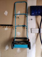 Full view of blue Gardena manual lawn mower hung on garage wall