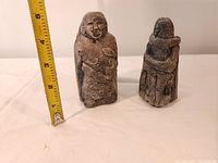 Two Irish Geltstone statues side by side, about 3-4 inches tall with a measuring tape for size reference showing approx. 3.75 inches