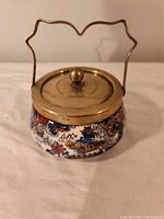 Front view of the ceramic jar with brass lid and handle, showing detailed pattern and ornate handle.