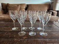 Seven crystal wine glasses grouped on wooden table showing cut leaf pattern
