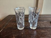 Set of four clear crystal water glasses with intricate cut design on a wooden surface.