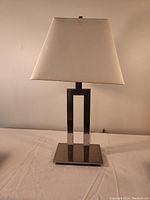 Metal table lamp with rectangular beige fabric shade on a white surface against a light wall.