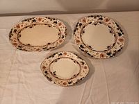 Three decorative plates with hand-painted floral patterns and ornate motifs arranged on a cloth surface.