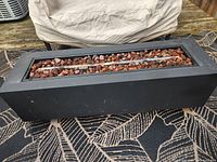 Front view of matte black rectangular propane fire pit with central burner and lava rocks