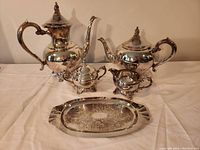 Full view of the silver-plated tea set including coffee pot, teapot, creamer, sugar bowl, and serving tray with ornate engraving.