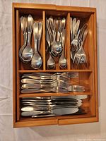 Top view of the flatware set organized in a wooden drawer tray, showing forks, spoons, knives, and other utensils.