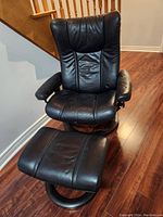 Front view of the black leather Stressless recliner chair paired with ottoman on wood flooring