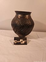 Photo of dark metal vase with detailed raised leaf pattern and flared opening