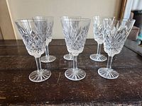 Six clear vintage Waterford crystal wine glasses arranged on wooden surface, showing cut crystal patterns.
