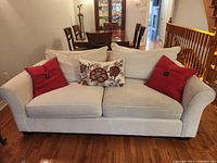 Front view of white upholstered sofa with rolled arms, two seat cushions, three decorative throw pillows on wood floor
