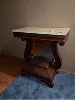 Full side view of the antique table showing white marble top and wooden base with curved mirror panel