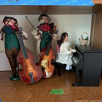 View of all six Byers Choice Carolers figurines, three musicians holding string instruments, one female playing piano, piano and decorative basket.