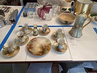 Photo showing the chocolate pot set including six cups and saucers arranged around a serving plate, all decorated with pine cone and pine needle patterns.