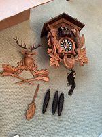Top down view of cuckoo clock and accessories laid out showing deer carving, bird carving, weights, pendulum and chains.