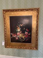 Full view of framed floral still life artwork on wall featuring gilded frame and floral fruit composition.