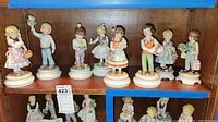 Shelf with 10 Blumenkinder figurines, mostly children holding flowers, dressed in various pastel colors, various poses