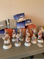 View of all 10 porcelain Blumenkinder figurines arranged on table with original Goebel boxes behind them.