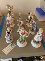 Overview of all twelve Goebel Blumenkinder porcelain figurines arranged on a table, showing variety in size, colors, and poses.