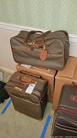 Two pieces of Hartman vinyl luggage, duffel bag on top of rolling suitcase with visible leather handles and patterned vinyl material.