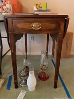Front view of drop-leaf table showing drawer, brass pull, tapered legs and drop leaves.