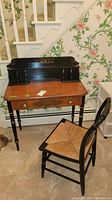 Full view of the Hitchcock style desk and matching chair placed by floral wallpapered wall and staircase