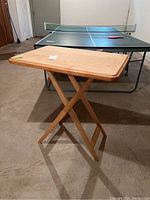Wooden folding tray table standing on basement floor near a ping pong table.
