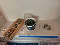 Wide view of marbles in plastic tub, wooden box with compartments, and small baggie all placed on a shelf.