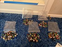 Five small plastic baggies filled with assorted glass marbles laid out on blue carpet.
