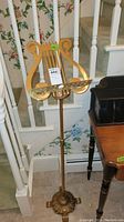 Full view of the gold metal music stand showing the entire structure from base to top with lyre-shaped sheet holder.