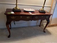 Full view of a wooden hall table with two drawers, brass hardware, curved cabriole legs, and decorative scalloped edges on apron and tabletop.