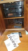 Wide shot of stereo built into wooden cabinet showing stacked Pioneer components, amplifier, cables inside shelf, manuals and remote on floor