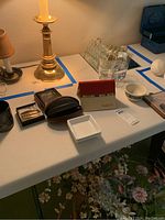 Table setup showing various items including lamps, wallet, shakers, coaster carrier, small mirror, dish, and glasses arranged neatly on a white folding table.