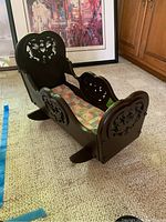 Side angled view of the Victorian wooden cradle showing dark wood finish and patchwork quilt inside.