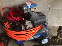 Overall view of Campbell Hausfeld air compressor with multiple air hoses coiled around it and boxed air regulator on top