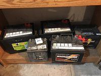 Five automotive batteries on wooden shelf: three in back row, two in front